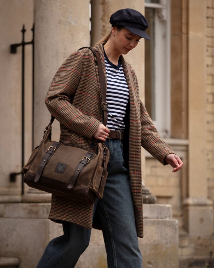 Close-up of a dark oak messenger bag made of waxed canvas and leather worn with a plaid coat.