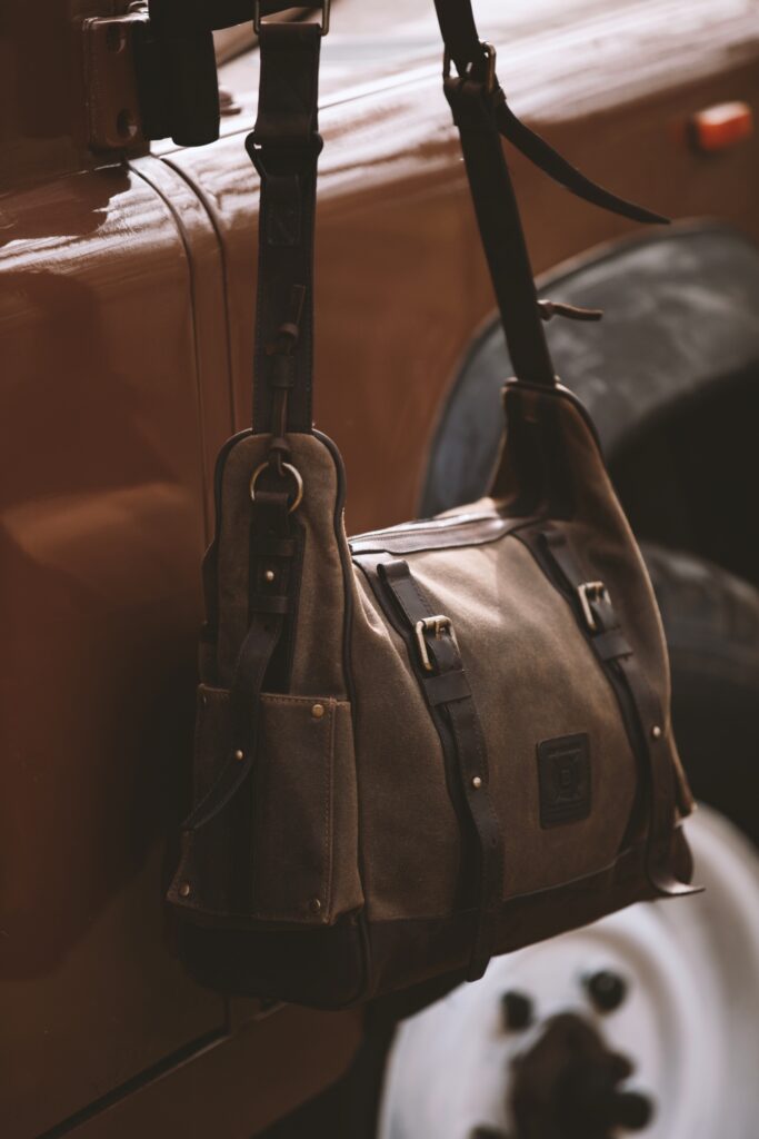 Close-up of a dark oak messenger bag made of waxed canvas and leather worn with a plaid coat.